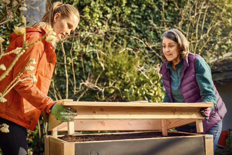 Zwei Frauen montieren ein Hochbeet im Garten.