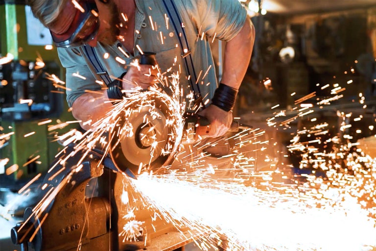 Mann benutzt einen Winkelschleifer beim Bearbeiten von Metall mit Funkenflug
