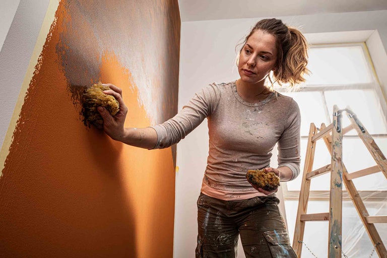 Femme décorant un mur avec une éponge et de la peinture, avec une échelle dans la pièce