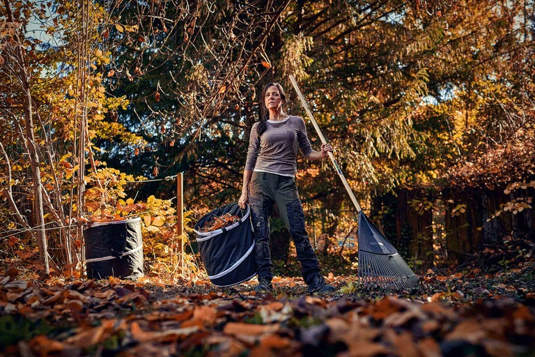 Frau mit Rechen und Laubsack im herbstlichen Garten