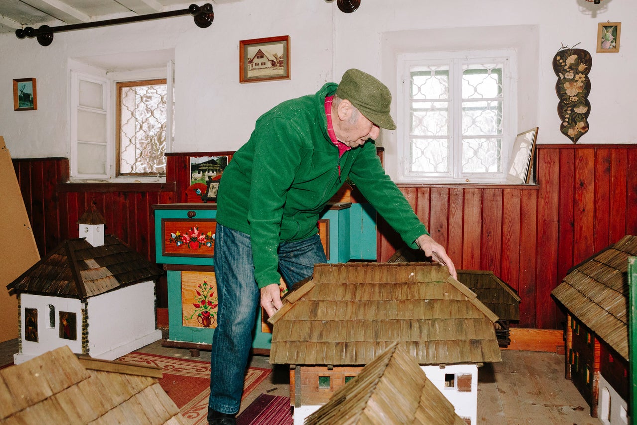 Un homme examine des maisons miniatures dans une pièce avec des fenêtres et des meubles peints.