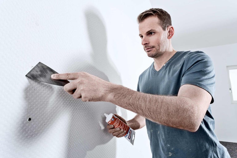 Un homme remplit un trou dans un mur avec du mastic et un couteau à mastic