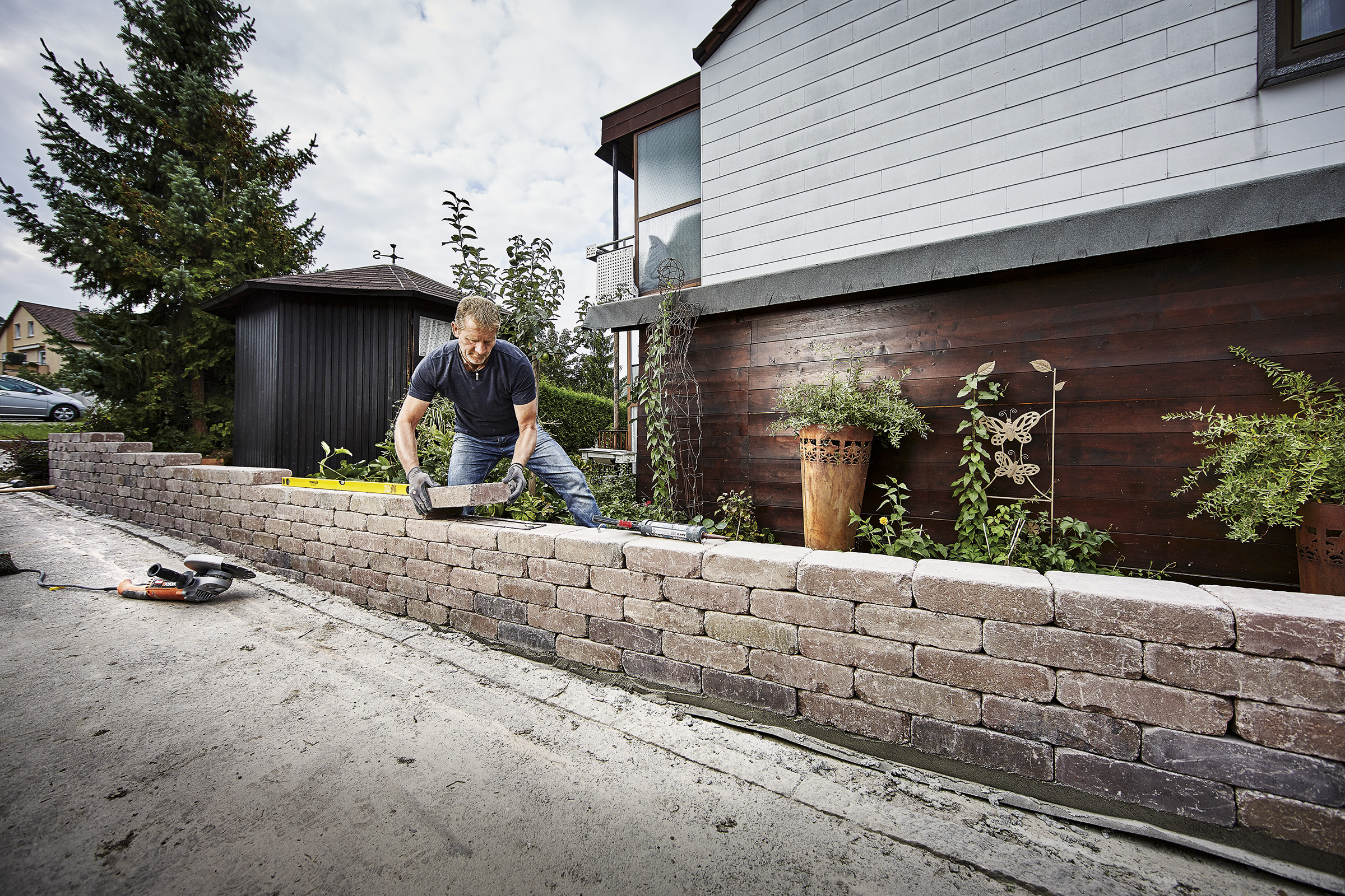Un homme construit un mur de pavés dans le jardin.
