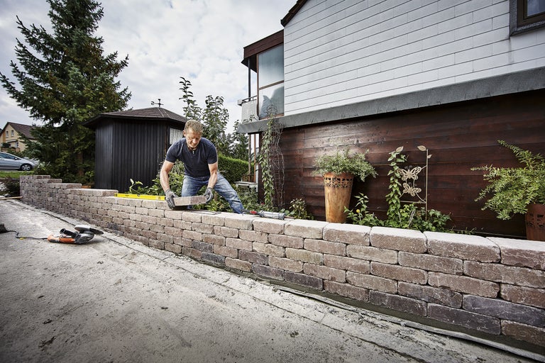 Mann baut eine Mauer aus Pflastersteinen im Garten.