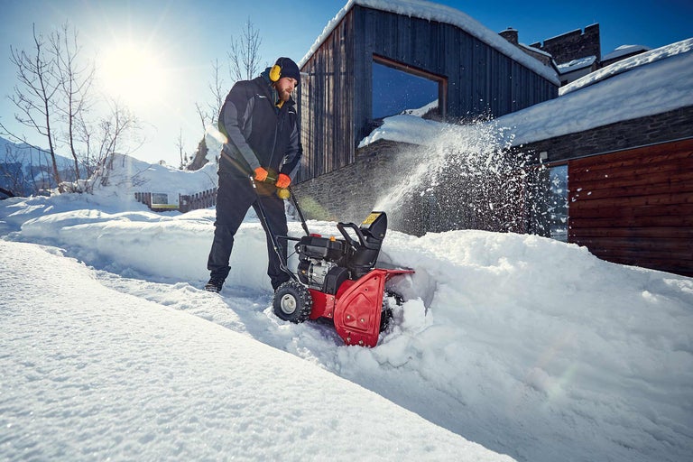 Mann räumt mit einer Schneefräse Schnee vor einem Haus
