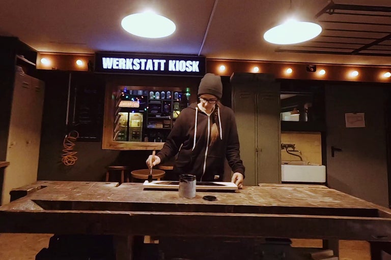 Une femme peint une planche de bois dans un atelier.