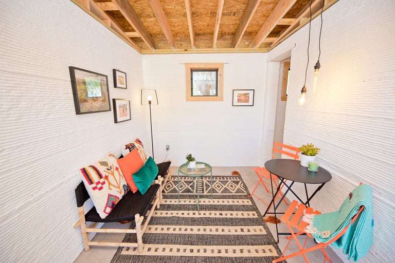 Intérieur avec canapé, table, chaises et tapis dans une maison aux murs imprimés en trois dimensions.