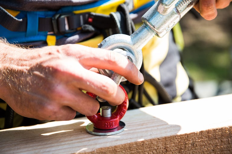 Eine Person verbindet eine Ringschraube mit einem Schäkel an einem Holzbalken.