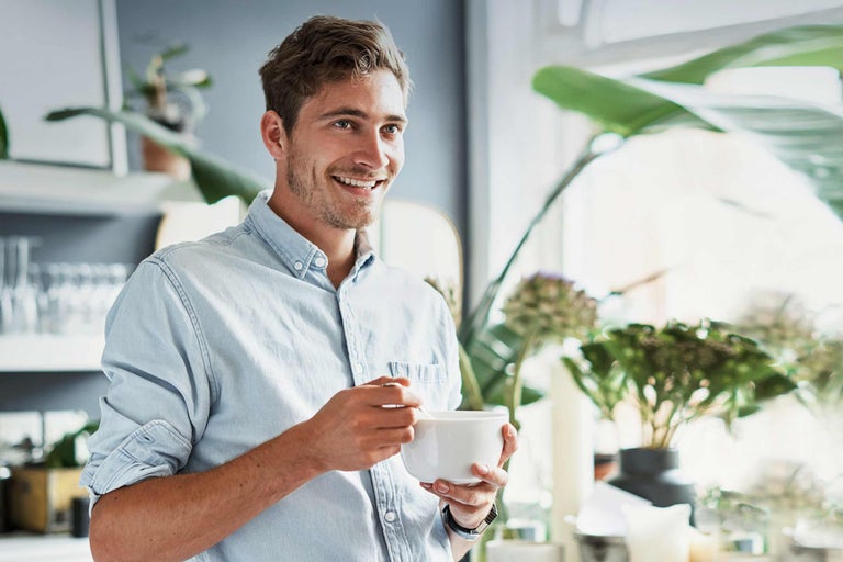Homme souriant avec un bol de céréales dans une cuisine lumineuse avec des plantes