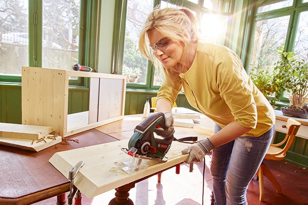 Frau sägt Holzbrett mit Stichsäge in Werkstatt für Heimwerkerarbeiten