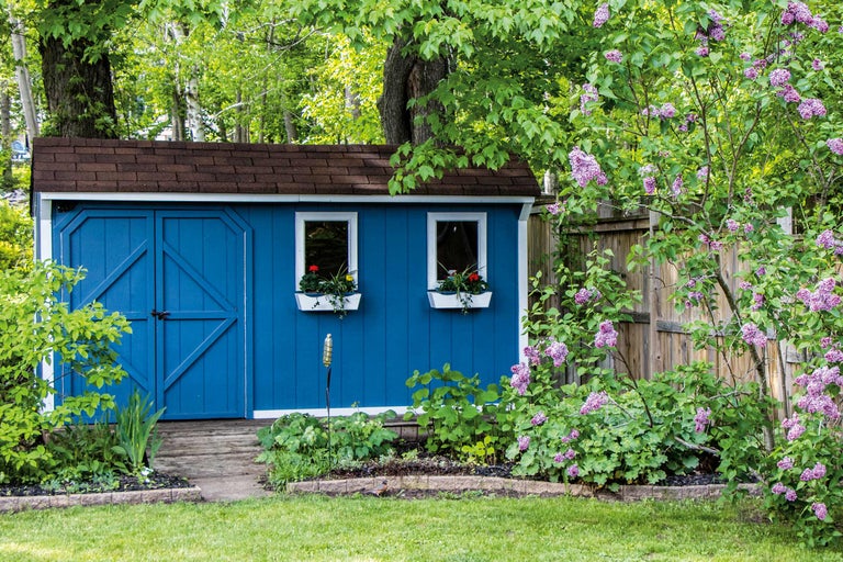 Vue de jardin avec cabanon bleu, fenêtres avec jardinières et arbustes à fleurs lilas