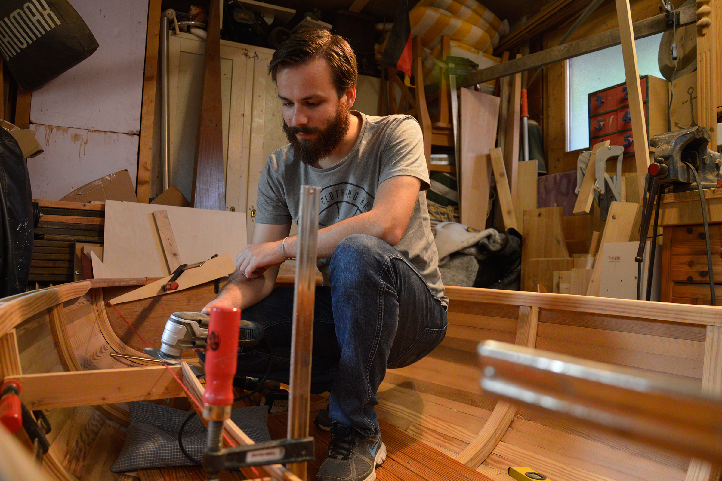 Mann arbeitet an einem Holzboot in einer Werkstatt mit Werkzeugen