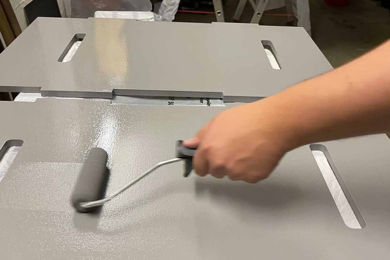 Une personne peint des panneaux en bois avec un rouleau à peinture