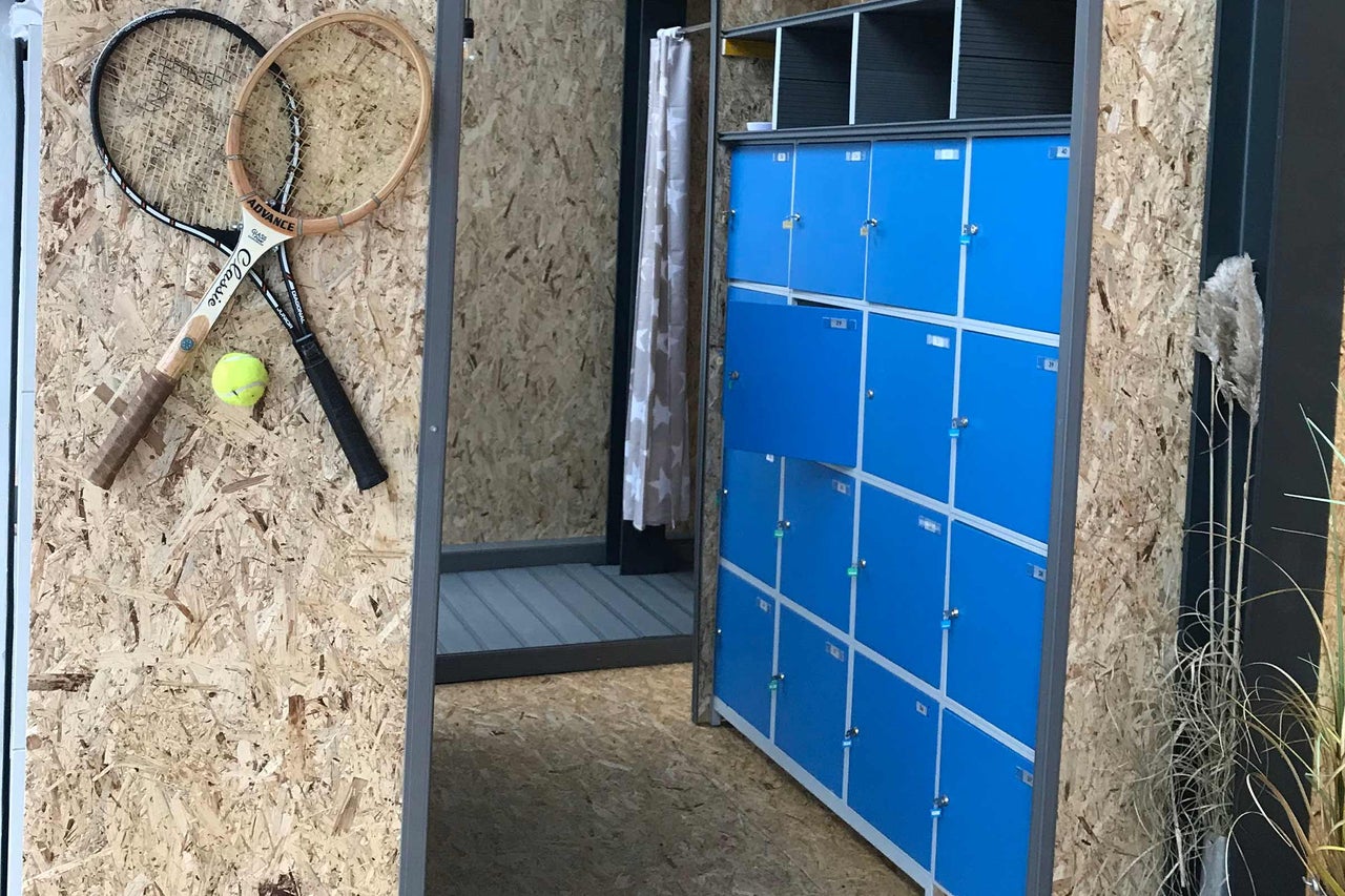 Innenraum mit blauen Schliessfächern, Umkleidekabine mit Vorhang, zwei Tennisschlägern und einem Tennisball