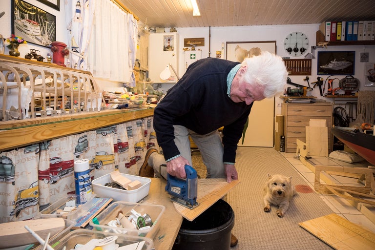 Mann arbeitet mit Stichsäge in Werkstatt, Hund liegt am Boden