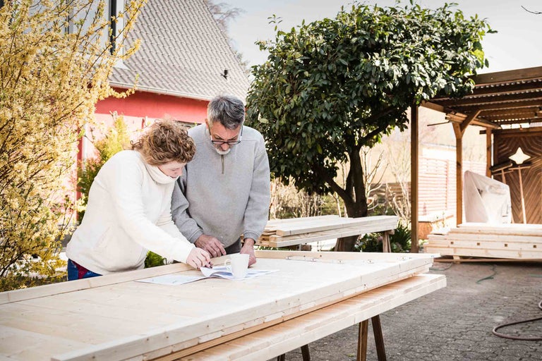 Deux personnes regardent des plans de construction sur une table avec du bois dans le jardin.