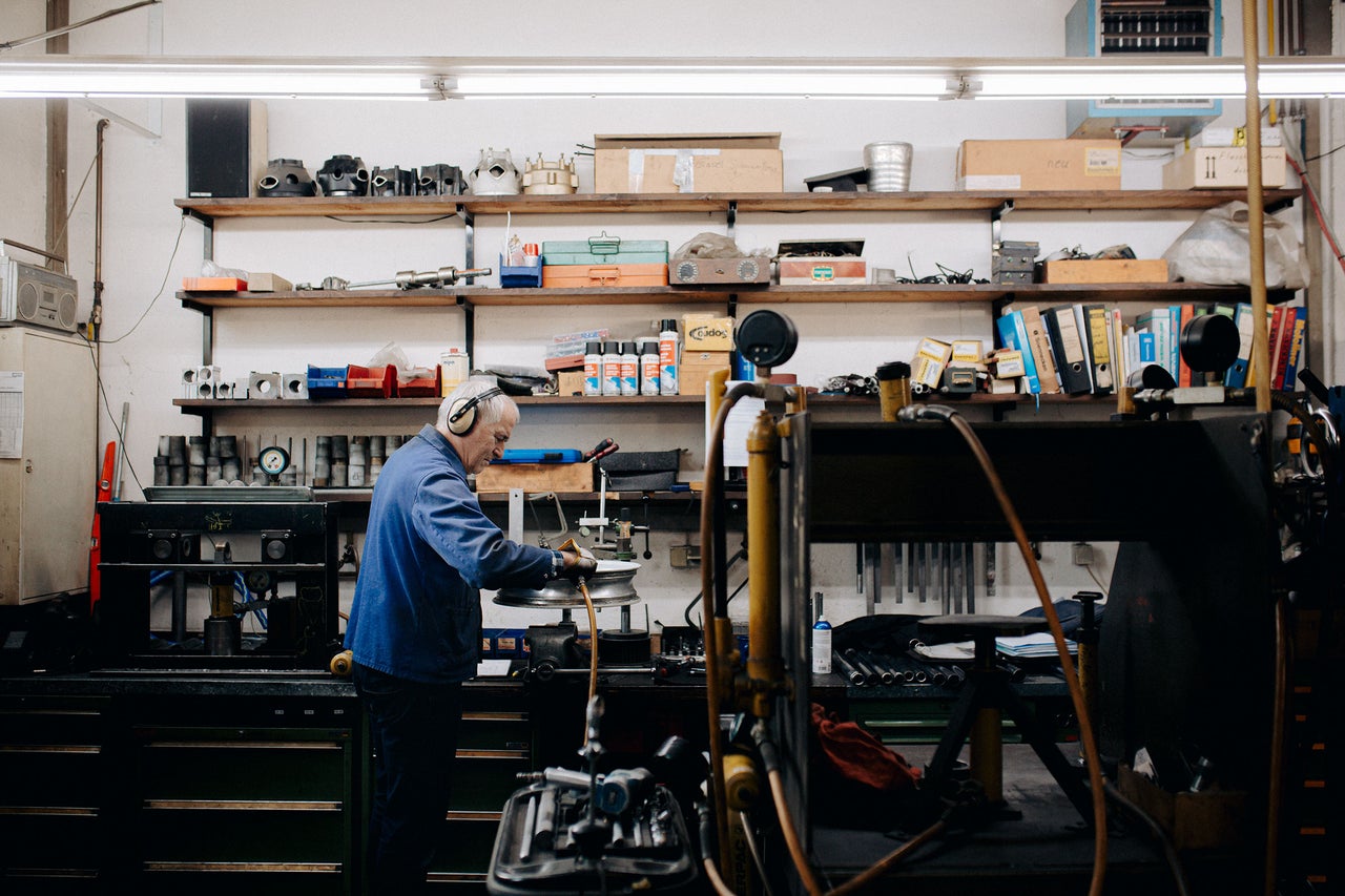 Werkstatt mit einem Arbeiter, der einen Reifen bearbeitet und Regalen voller Werkzeuge und Materialien