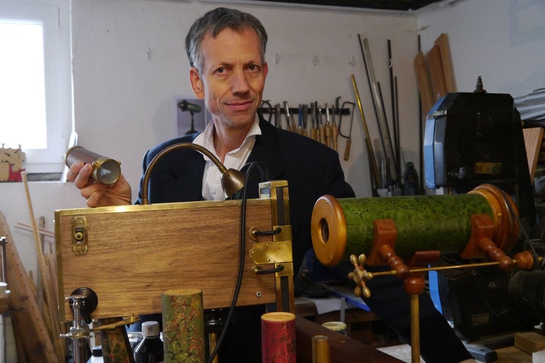 Homme présentant un télescope artisanal en bois et métal dans un atelier