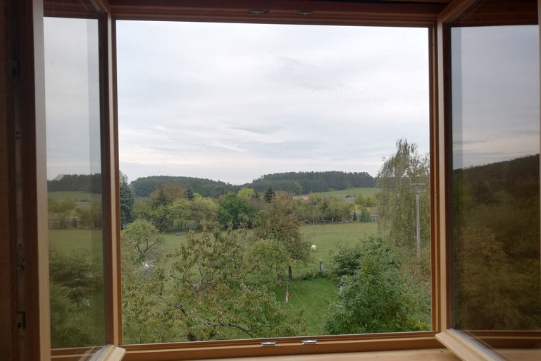 Geöffnetes Fenster mit Blick auf eine ländliche Szene mit Bäumen und Wiesen