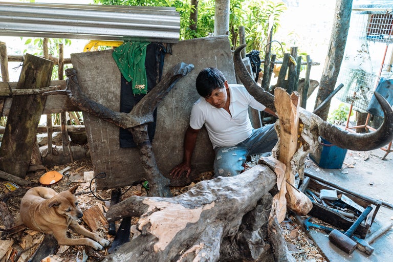 Un homme sculpte une sculpture en bois avec des outils à côté d'un chien