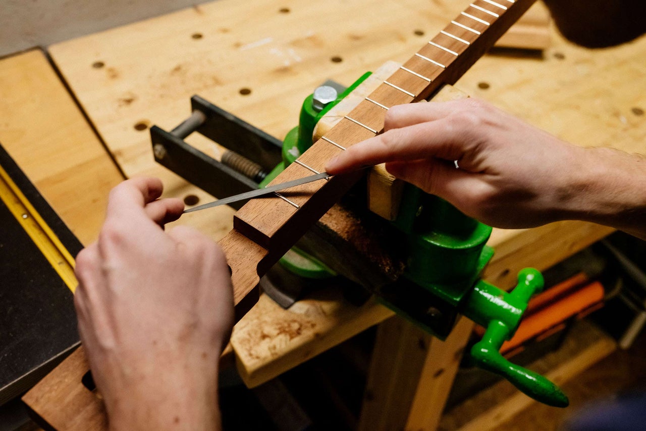 Une personne travaille avec une lime sur un manche de guitare fixé dans un étau.