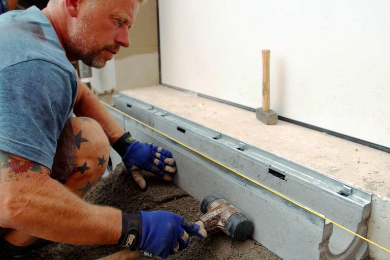 Un homme pose un caniveau de drainage avec un marteau sur du gravier