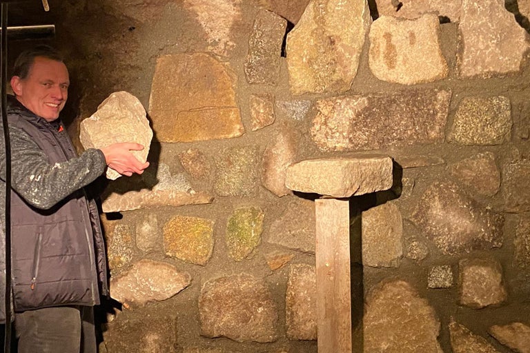 Homme tenant une pierre devant un mur de pierres