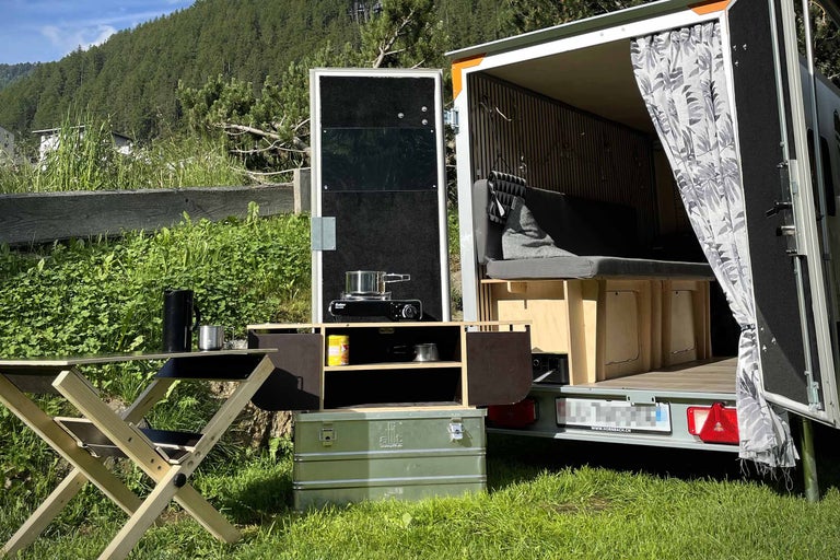 Caravane de camping avec cuisine, table et espace de rangement à l'extérieur.