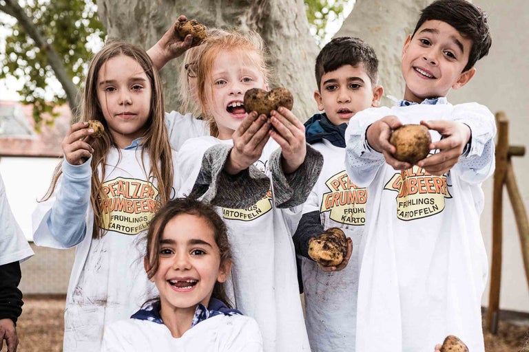 Un groupe d'enfants présente des pommes de terre primeur devant un arbre.
