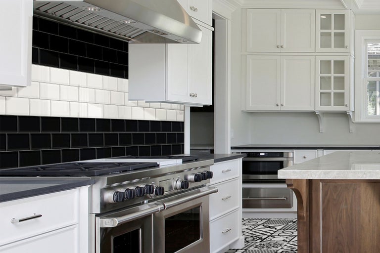 Cuisine lumineuse avec plan de travail, hotte aspirante, cuisinière, armoires blanches et carrelage en noir et blanc