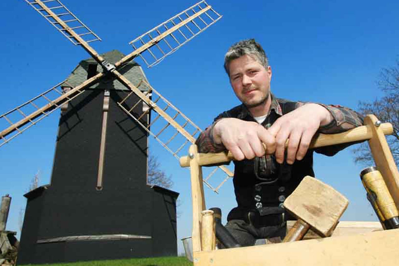Charpentier en tenue de travail traditionnelle avec un moulin à vent en arrière-plan