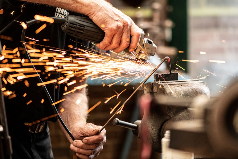 Une personne meule une pièce métallique avec une meuleuse, des étincelles jaillissent.