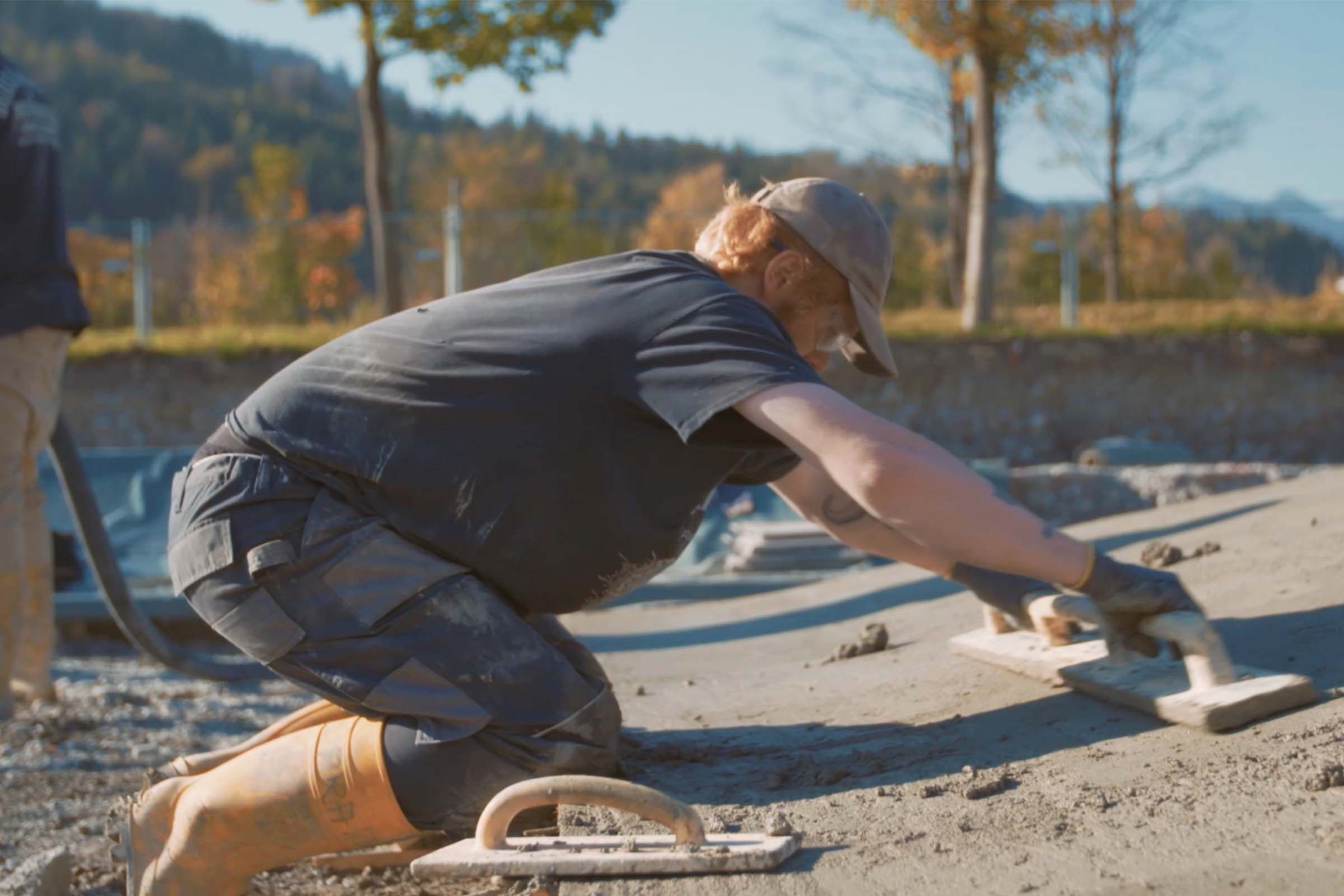 Un ouvrier du bâtiment lisse une surface en béton à l'aide d'une taloche.