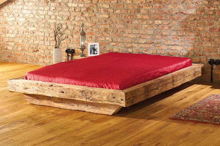 Lit en vieux bois avec literie rouge devant un mur de briques