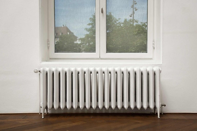 Weisser Heizkörper unter einem Fenster auf einem Holzboden