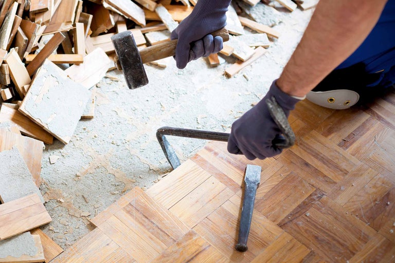 Un artisan retire un plancher en bois avec un marteau et un burin.