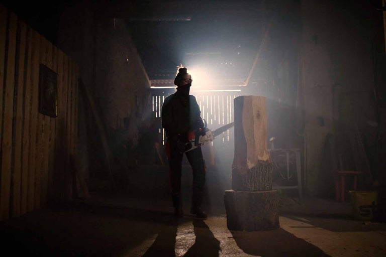 Mann mit Kettensäge, der einen Holzstamm in einem dunklen Raum bearbeitet
