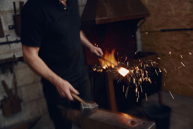 Forger travaillant le métal incandescent avec un marteau sur une enclume dans la forge