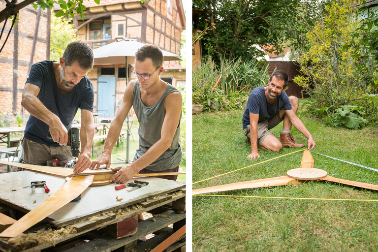Zwei Männer bauen eine Windkraftanlage im Garten. Einer misst die Rotorblätter, während der andere die Teile zusammenschraubt.