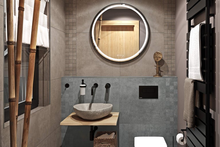 Modernes Badezimmer mit rundem beleuchtetem Spiegel, Naturstein-Aufsatzwaschbecken auf Holzkonsole, schwarzen Wandarmaturen und grauen Fliesen.