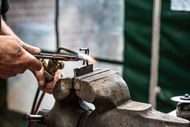 Un homme soude du métal avec un chalumeau, maintenu dans un étau.