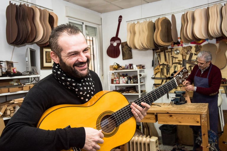 Mann spielt Gitarre in einer Werkstatt mit Gitarrenbaumaterialien und Werkzeugen.