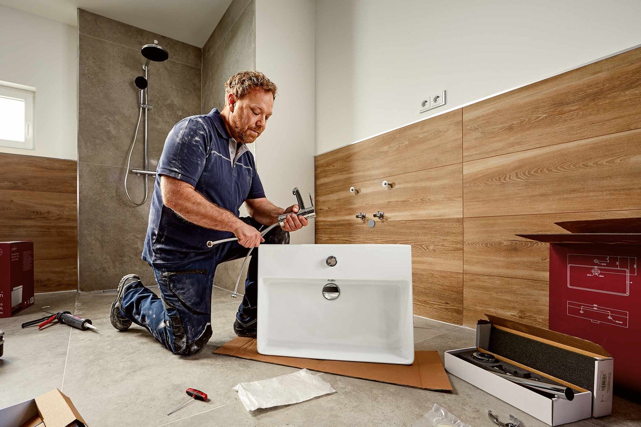 Un installateur installe un lavabo dans une salle de bains avec douche.