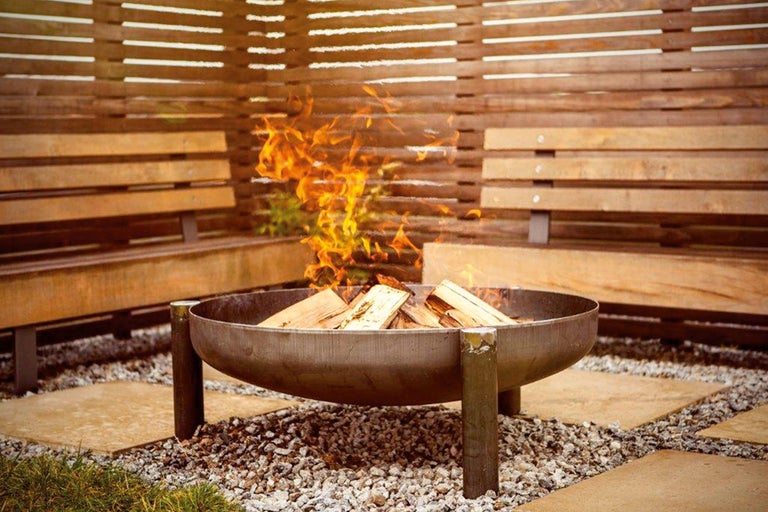 Brasero avec bois et flammes dans un jardin avec bancs en bois et sol en pierre