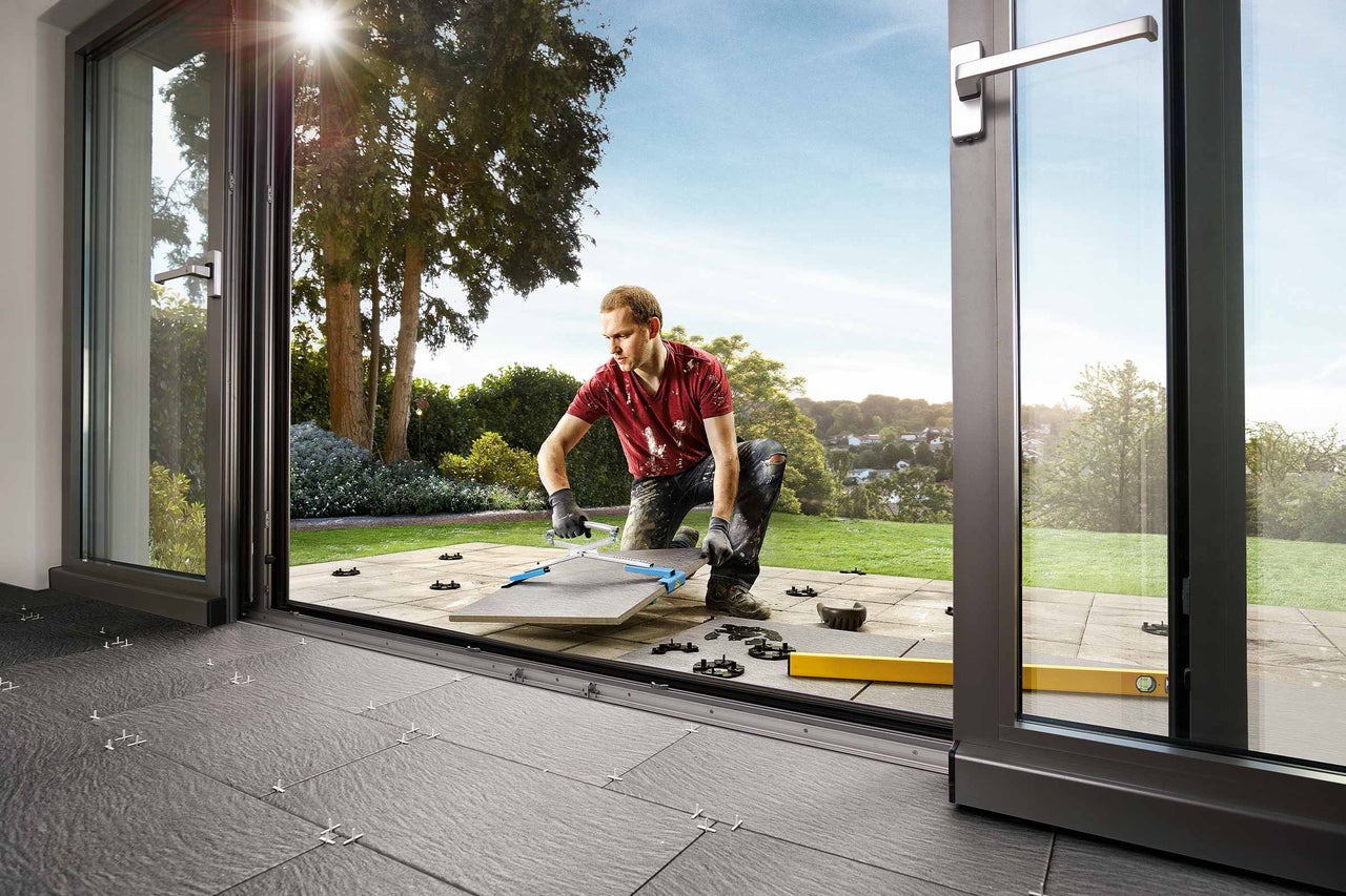 Mann verlegt Fliesen auf einer Terrasse mit Hilfe eines Fliesenverlegesystems