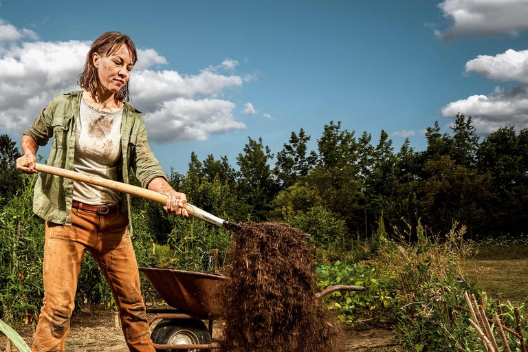 Une femme déplace de la terre avec une pelle dans une brouette dans un jardin.