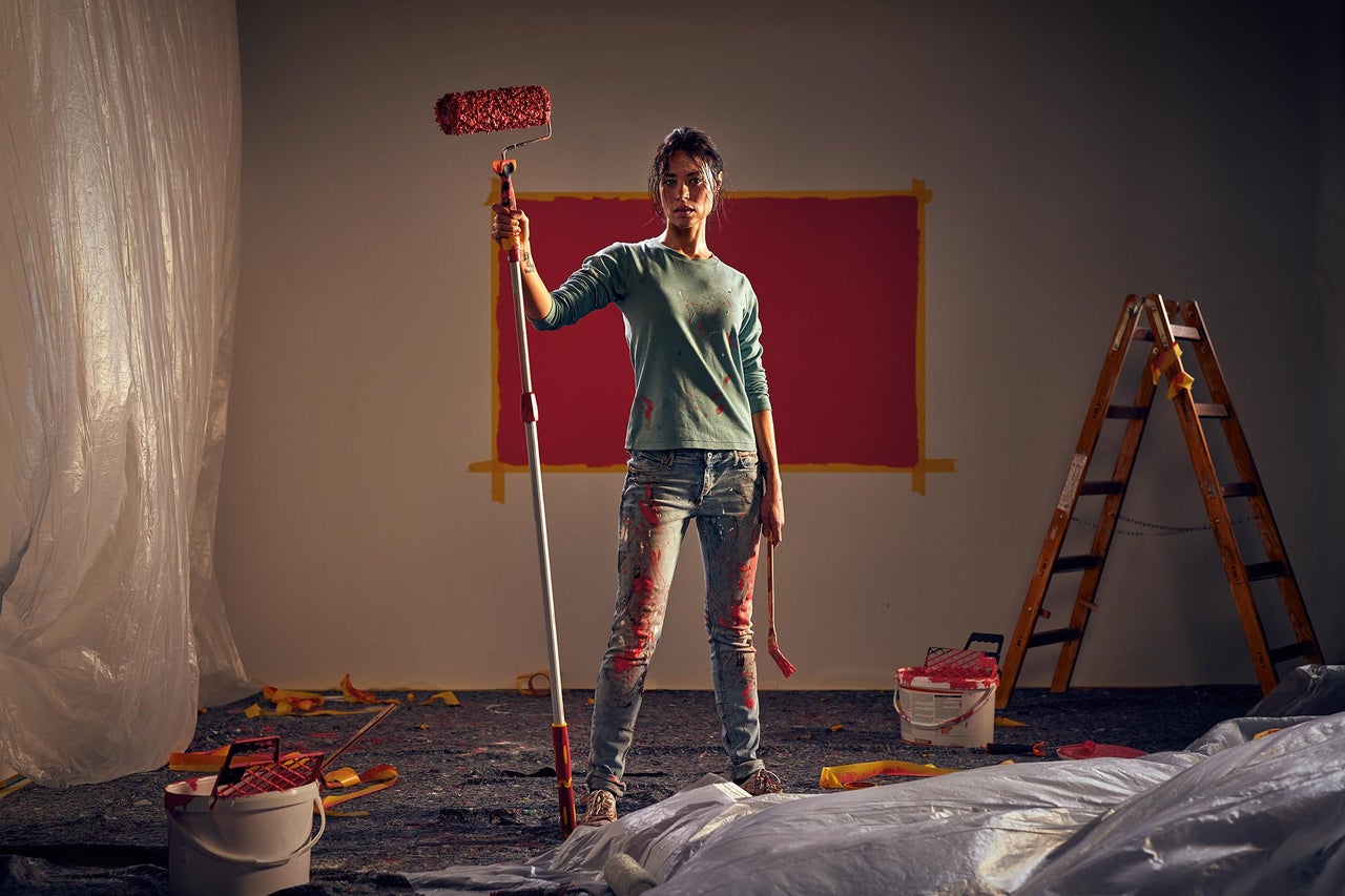 Femme avec rouleau à peinture dans une pièce à rénover avec bâche de protection et échelle