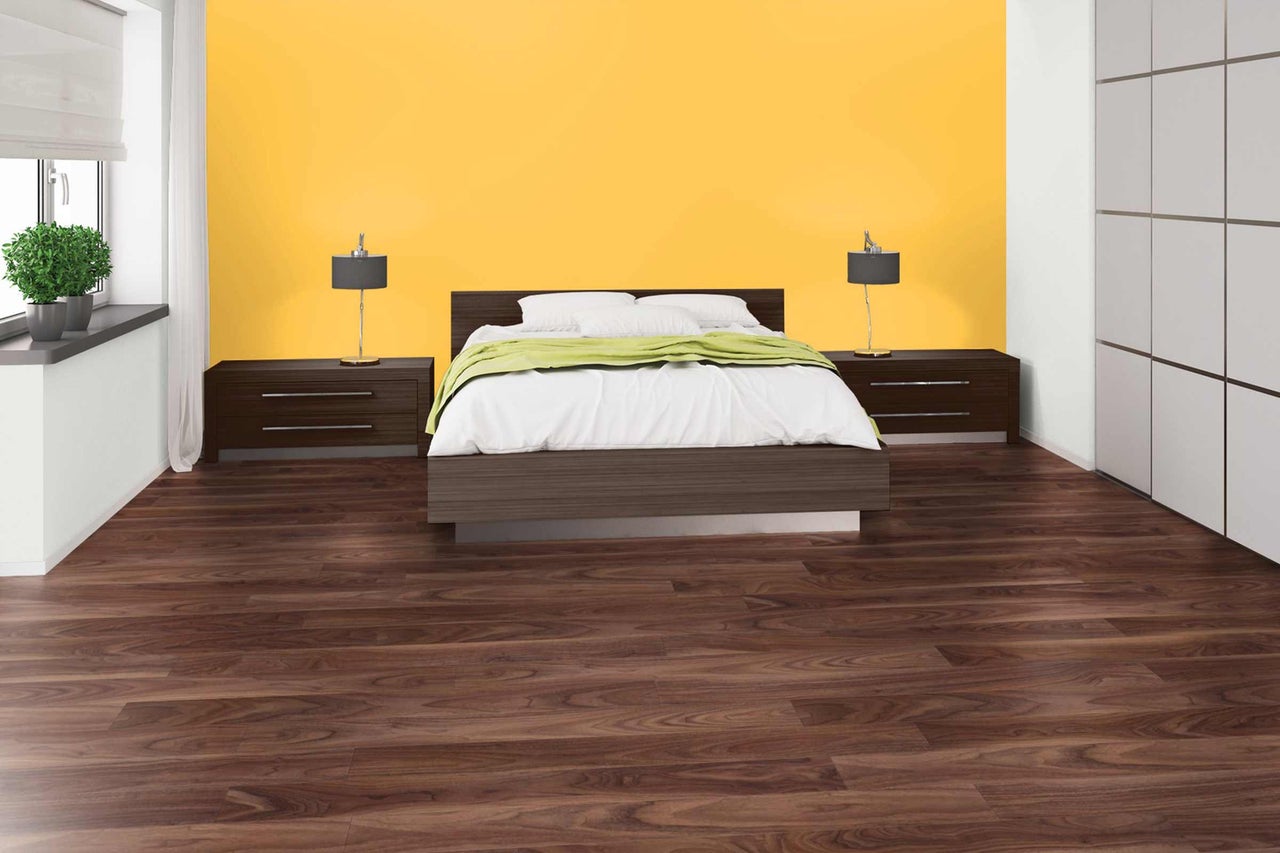 Chambre avec lit, tables de chevet, lampes, sol stratifié et mur jaune