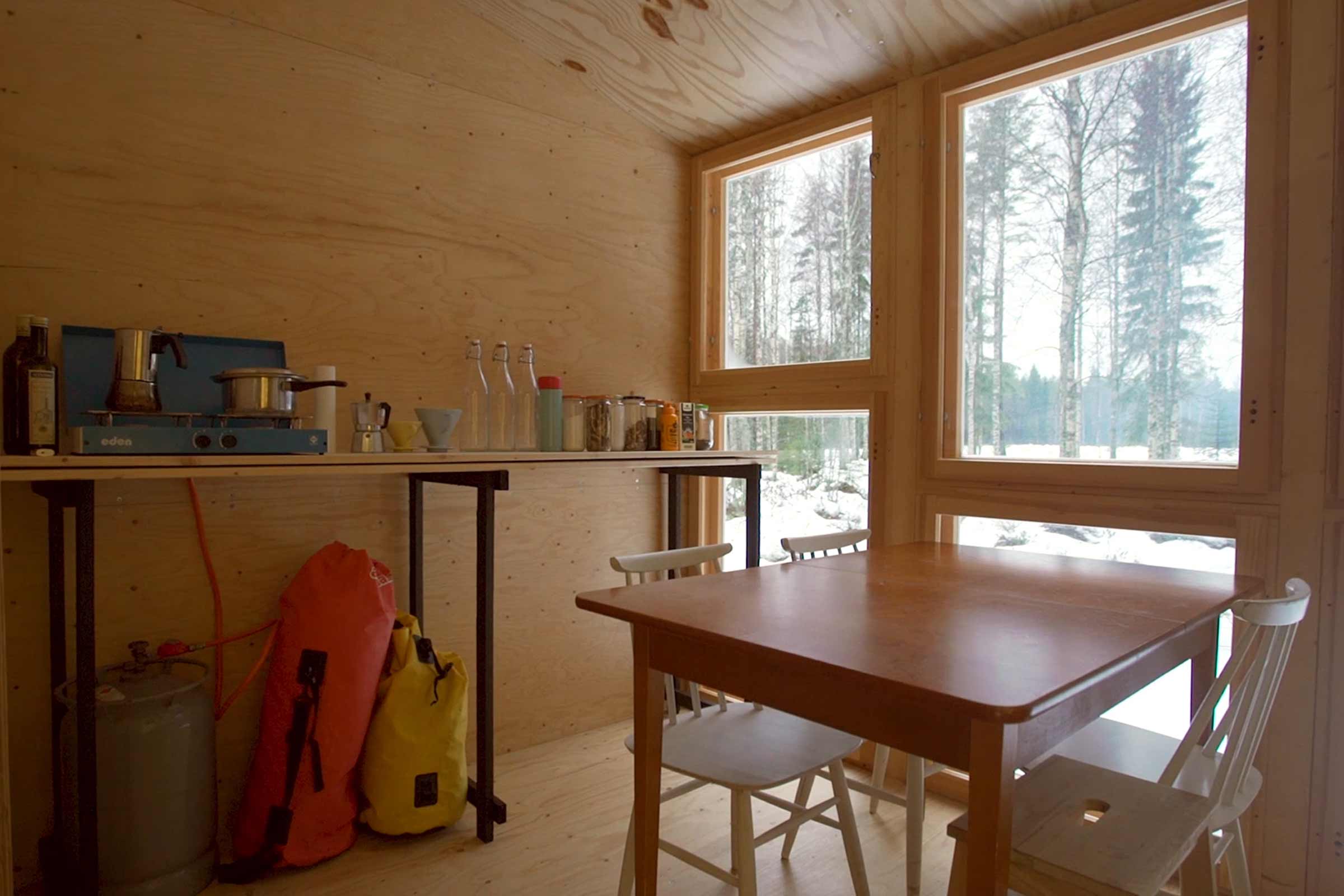 Vue intérieure d'une pièce avec une table, des chaises et des étagères devant la fenêtre.
