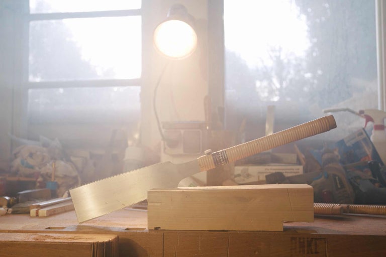 Scie japonaise coupant un morceau de bois sur un établi.